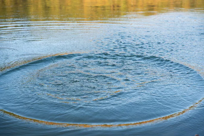 Circular water ripples and bubbles effect. Water ripples and round droplets on blue sea texture pattern background. Liquid motion on calm lake surface. Ring affect, circles