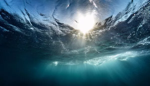a shot taken from beneath the surface of the sea looking up at the sky the light patch is the sun overhead and through the surface it is possible to see the rain falling hard on the water